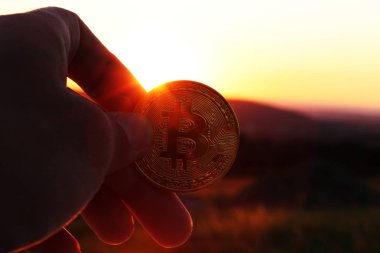 Güzel bir altın bitcoin içinde el bazı yatırım danışmanı veya bankacı günbatımı ve dağ. Arka plan bulanıklık