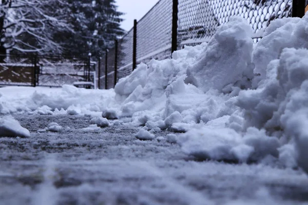 A snow pile near fence. Trying shoveling snow from driveway. Twenty centimetres snow coverlet must be cleaned.