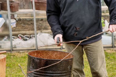 Büyükbaba siyah ceketli siyah bir varil içine dalları keser. Bahçesinde bahar ilk iş. Dalları kuru erik. Bahar çalışma. 