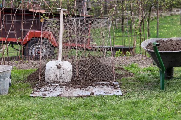 Herramientas de jardín de trabajo. Pala apoyada contra el tamiz. Carretilla llena de tierra. Cubo escondido en la esquina. Utensilios importantes para el trabajo en el jardín. Trabajo de verano —  Fotos de Stock