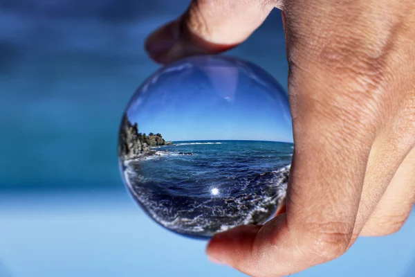 Bola de cristal com recleção de Afrodite praia de banho à luz da manhã. Bola de vidro / lente segurando na mão com azul, mar claro. Céu é sem nuvens. Litoral no Parque Nacional da Península de Akamas, Chipre — Fotografia de Stock