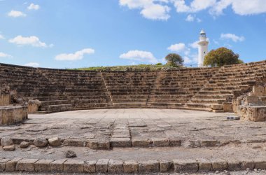 Baf bazı vesileyle Roma amfitiyatro. Pafos, Kıbrıs'ta arka planda beyaz deniz feneri ile Antik tiyatro. Pafos'ta birçok anıtla arkeoloji parkı