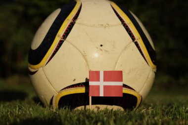 Çim ve futbol topu ile Danimarka bayrağı. Şampiyonluk 2022. Euro 2020. Futbol sahasında devlet sembolü. Futbol çevresinde Danimarka ulusal bayrağı