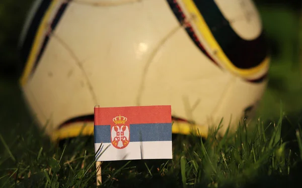 Flag of Serbia between stems of grass and in the background wonderfull classic ball. World Championship 2022. Euro 2020. Serbian state symbol. International match