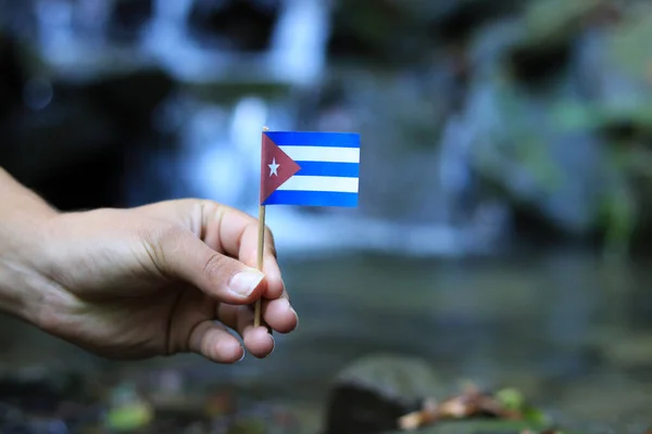 Bandiera nazionale di Cuba su bastone di legno. Giovane ragazzo tiene athem nazionale vicino alla cascata sul torrente in autunno volte. Concetto di umanità e natura. Repubblica di Cuba in mano. Bandiera per il pacchetto — Foto Stock