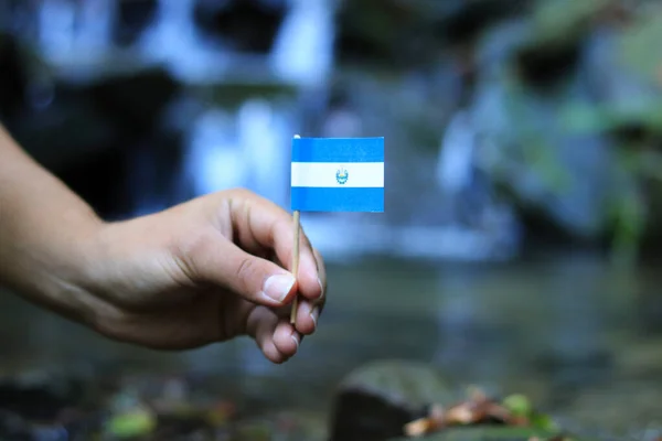 Tiener toont de nationale vlag van El Salvador. Kleur man houdt houten stok met papier in vorm vlag. Vlag Republiek El Salvador op pakketje. Concept van menselijkheid en natuur. — Stockfoto