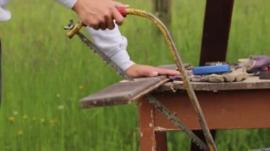 Genç çırak bir el testeresini doğru kullanmayı ve düz kesmeyi öğreniyor. Tahtayı verilen boyuta göre kesiyorum. Tahtayla çalışmak. Parmaklar için tehlikeli bir iş. Kesin konsantrasyon