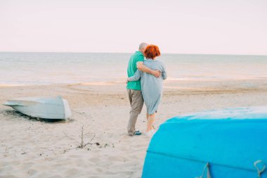 Romantik üst düzey çift el ele tutuşarak deniz kıyı yürüyüş açık bir kadeh. Komuta sizde ve sahilde birlikte günbatımında yürüyen kadın.