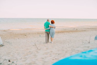 Romantik üst düzey çift el ele tutuşarak deniz kıyı yürüyüş açık bir kadeh. Komuta sizde ve sahilde birlikte günbatımında yürüyen kadın.