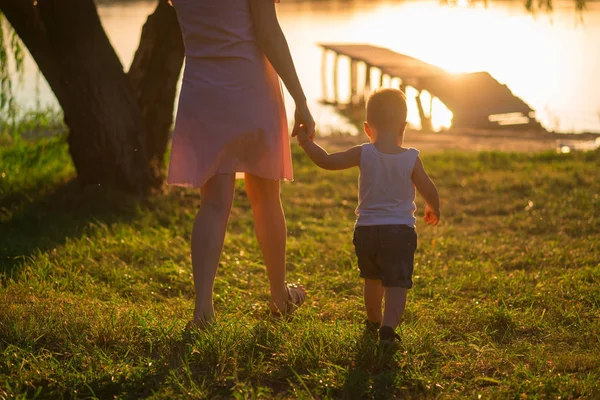 güzel anne iskelede ilk adımları ile onun küçük oğlu ile yaz saati, gün batımında yürüyor