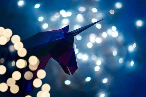 Fantastic photo of the silhouette of a unicorn on the background of a bokeh from the lights of a garland, a magic unicorn made of foil on a blue background with a place under the text