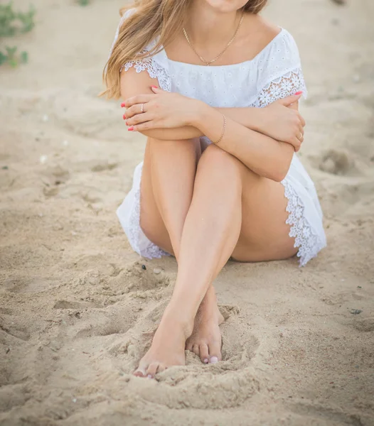 Piękny model w białej sukni siedzi seksualnie na piasku na plaży — Zdjęcie stockowe