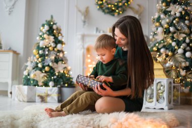 Anne oğlu bir hediye verir. küçük oğlu olan genç bir anne rahat bir şömine ve bir Noel ağacı arka plan üzerine koyun kılığına üzerinde dinlenmiş. aile tatilleri