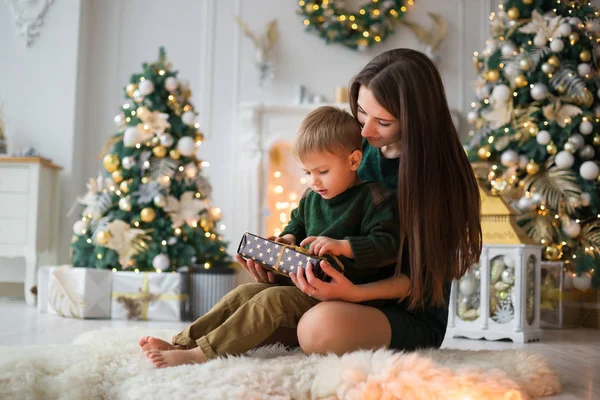 Anne oğlu bir hediye verir. küçük oğlu olan genç bir anne rahat bir şömine ve bir Noel ağacı arka plan üzerine koyun kılığına üzerinde dinlenmiş. aile tatilleri