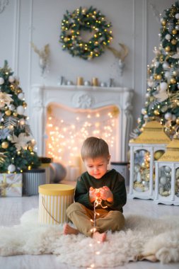 küçük çocuk komik yüz şömine Yılbaşı dekor, çelenk, Noel ağaçları, hediyeler ile arka plan üzerinde yapıyor. Mutlu Noeller