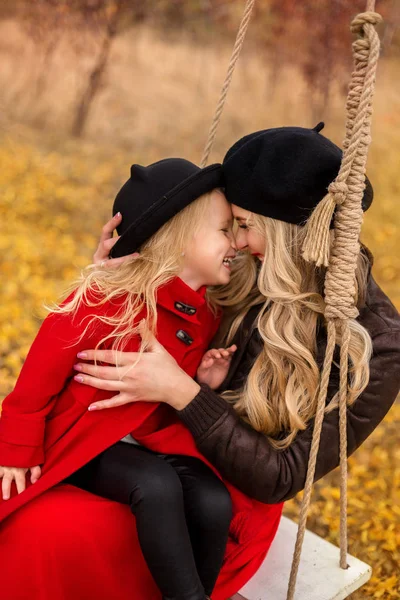 長い金髪を持つ非常に美しい若い母親カール彼女の金髪の若い娘を抱き締めると 彼らは秋の庭の背景に楽しそうに笑っています — ストック写真