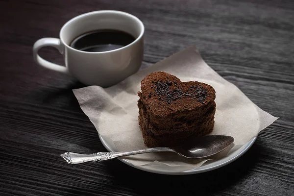 bir ahşap eski arka plan üzerinde beyaz bir daire hoş kokulu kahve yanında kalp şeklinde çikolata tatlı duruyor