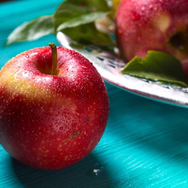 Bir tabak meyve yakınındaki mavi ahşap bir masa üzerinde su damlacıkları ile ıslak bir elma yatıyor