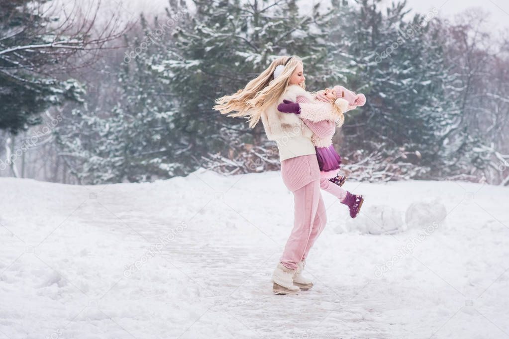 mum is spinning her daughter in her arms in a snowy park