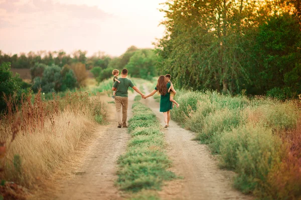 Concept vacances parc familial. Une famille de quatre maman, père tenant son fils, parents tenant un enfant main marchant au coucher du soleil — Photo
