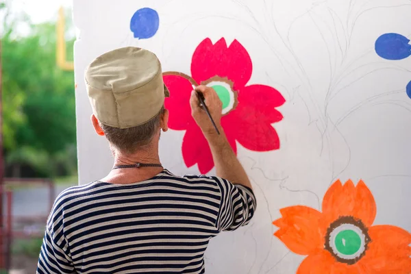 a man paints and paints paint a white wall with floral ornaments . summer