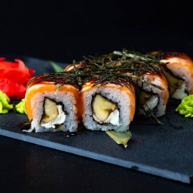 Suşi, Philadelphia usulü somon, füme yılan balığı, avokado, siyah arka planda krem peynir. Suşi menüsü. Japon yemeği. Philadelphia somonlu, füme yılan balığı, avokado, siyah arka planda krem peynir. Suşi menüsü. Japon yemeği..