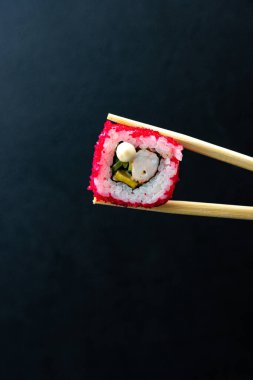 Japon suşisi kırmızı uçan balık yumurtası Tobiko havyarı koyu arka planda izole edildi. Kaliforniya usulü somon, salatalık, Norveç yosunu ve pilavına sarılmış avokado. Tabak izolasyonu