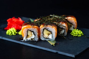 Suşi, Philadelphia usulü somon, füme yılan balığı, avokado, siyah arka planda krem peynir. Suşi menüsü. Japon yemeği. Philadelphia somonlu, füme yılan balığı, avokado, siyah arka planda krem peynir. Suşi menüsü. Japon yemeği..