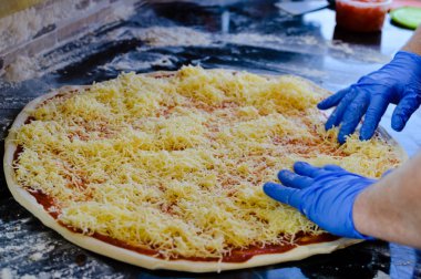 Closeup detail on hands of a chef making fresh Italian pizza cuisine, colorful tomatoes paste background