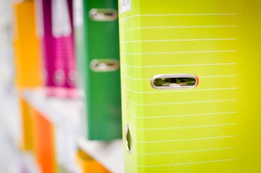 Close up on multicolored office folders on the bookshelf backgrounds. Many working stationery, stacked records. Different color spectrum documents. Educational or financial file-box object supplies