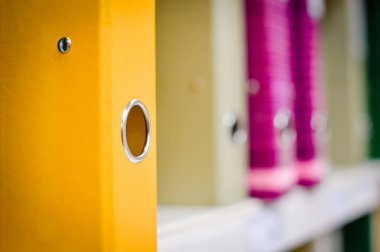 Close up on multicolored office folders on the bookshelf backgrounds. Many working stationery, stacked records. Different color spectrum documents. Educational or financial file-box object supplies