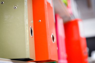 Close up on multicolored office folders on the bookshelf backgrounds. Many working stationery, stacked records. Different color spectrum documents. Educational or financial file-box object supplies
