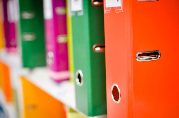 Close up on multicolored office folders on the bookshelf backgrounds. Many working stationery, stacked records. Different color spectrum documents. Educational or financial file-box object supplies
