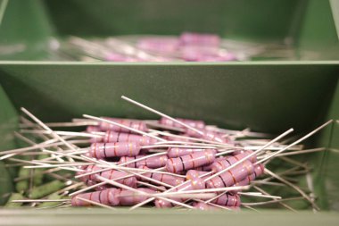 Yeşil plastik bir kutuda renkli bantlı birkaç mor karbon film rezistansının makro görüntüsü. Devrelerde, eğitimde ve prototipide kullanılan elektronik bileşenler