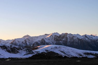 Güneş doğarken Pireneler 'deki karla kaplı dağların manzarası, tepeleri aydınlatan yumuşak altın ışıkla. Kış manzarası ve seyahat yeri