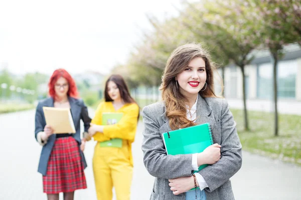 Una studentessa sorridente sta in piedi con una cartella. Concetto educativo, esami, amicizia e gruppo di persone — Foto Stock