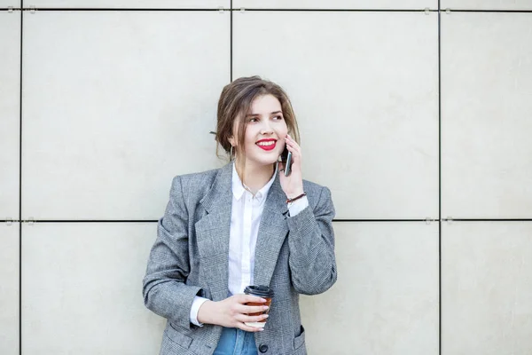 Femme adulte se tient près du mur avec du café. Communiquez par téléphone. Espace de copie. Concept de style de vie, urbain, entreprise, étude — Photo