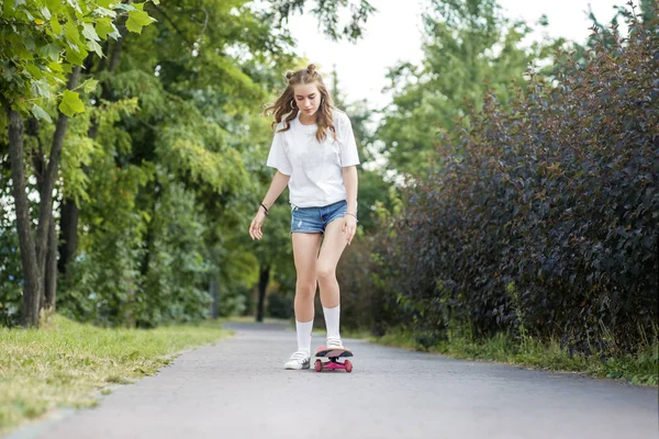 Happy girl goes for a drive on the skate board in the park. The concept of lifestyle, leisure.