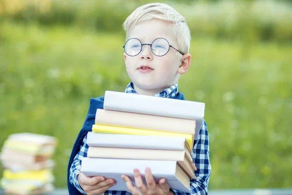 Egy kis okos gyerek tart sok tankönyvek a kezében. A tanulás, az iskola, az elme, az életmód és a siker fogalma. — Stock Fotó