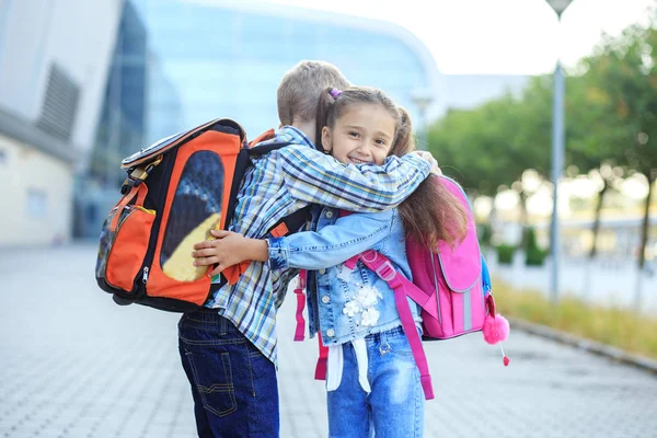 Glada barn kramar och skrattar nära skolan. Liten pojke och flicka — Stockfoto