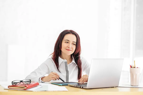 Una hermosa mujer está sentada en su escritorio y sonriendo. Concepto para negocios, trabajo, carrera . — Foto de Stock