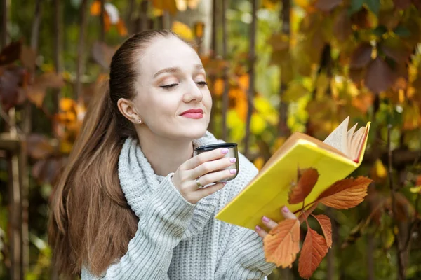 A girl reads a book and drinks tea from a thermos. The concept of lifestyle, autumn, relax and read.