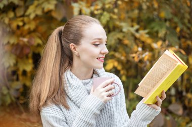 Bir kadın ilginç bir kitap okuyor. Sıcak kahve. Yaşam tarzı, sonbahar, rahatla ve oku..
