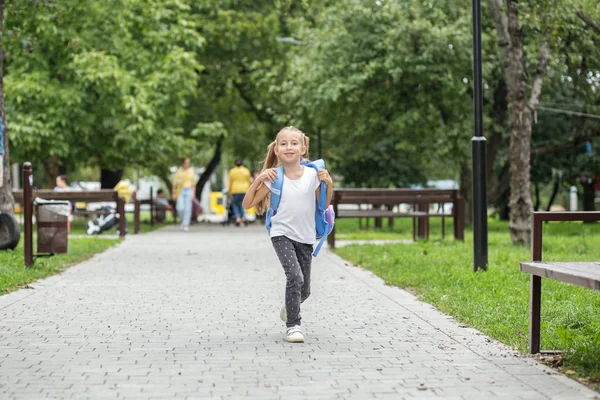 子供の女の子はリュックを持って学校を出る。学校、勉強、教育、友情の概念. — ストック写真