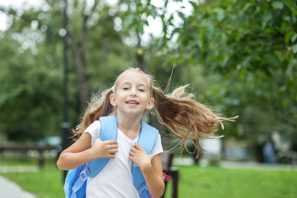 A kislány fut és mosolyog. Iskoláslány hátizsákkal. Az iskola, tanulás, oktatás, barátság fogalma. — Stock Fotó