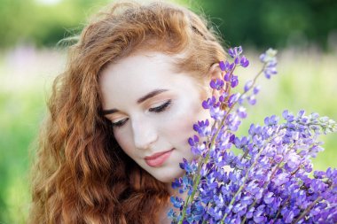 Güzel bir kadının portresi. Dalgalı kızıl uzun saçlar. Mor çiçekler. Yakın plan. Yavaş yaşam, organik kozmetik ve dijital detoks kavramları.