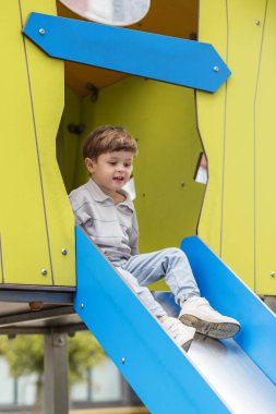 Genç çocuk hareketli bir oyun alanından kaymaya başlıyor. Şehir parkında aktif bir oyun sahnesinin tadını çıkarıyor..