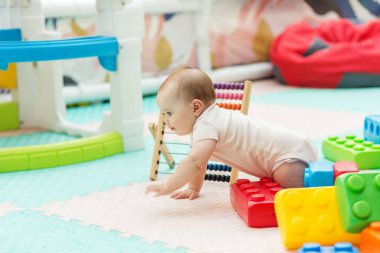 Bebek dört ayak üstünde oyuncak blokları ve abaküsü olan bir oyun alanını aydınlık, güvenli bir anaokulu ortamında keşfediyor. Ebeveynlik içeriği için ideal.