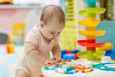 Bir duyusal masada renkli etkileşimli oyuncaklara odaklanmış bebek, oyun odasında bilişsel ve motor beceri geliştirmeyi teşvik ediyor.