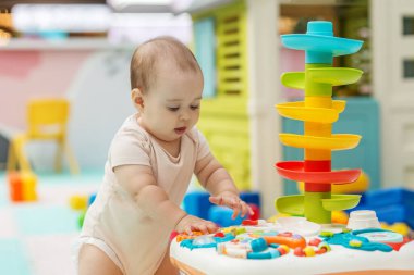 Çocukluğunda öğrenmesi için tasarlanmış güvenli, kapalı bir ortamda renkli bir duyusal aktivite masasıyla oynayan nişanlı erkek bebek..